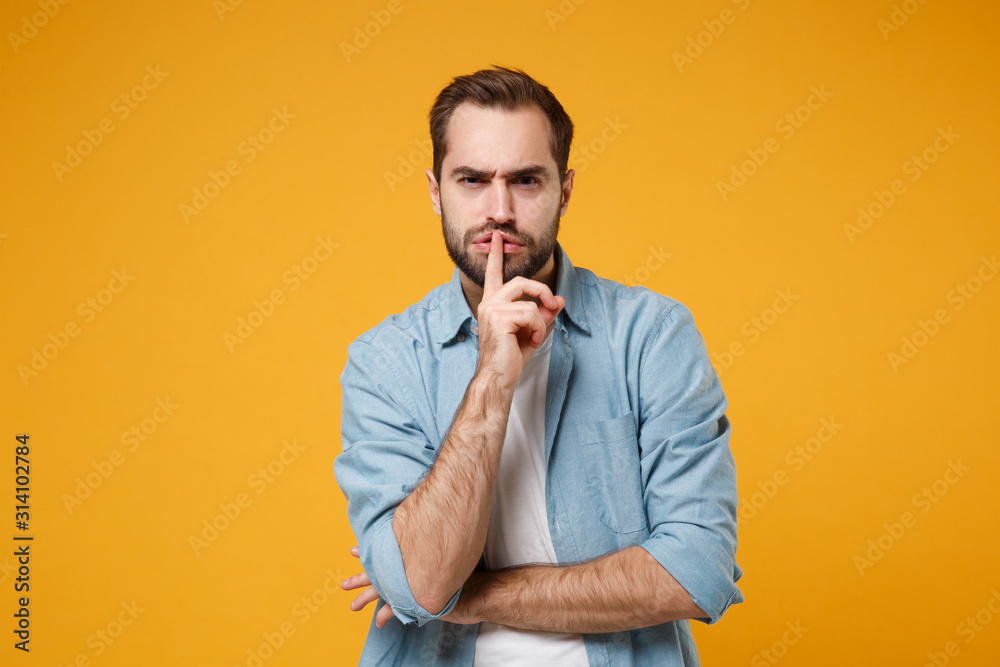 Secret young bearded man in casual blue shirt posing isolated on yellow orange wall background. People lifestyle concept. Mock up copy space. Saying hush be quiet with finger on lips shhh gesture. Secret young bearded man in casual blue shirt posing isolated on yellow orange wall background. People lifestyle concept. Mock up copy space. Saying hush be quiet with finger on lips shhh gesture.