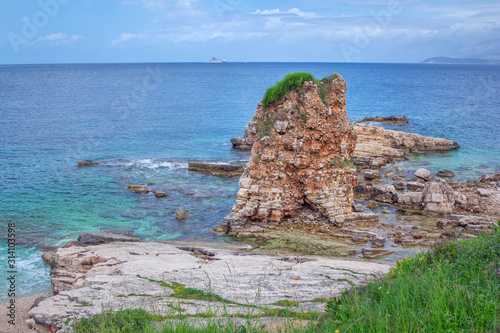 Beautiful landscape – turquoise sea water and cracked, ruined cliff, covered with green grass. Corfu Island, Greece. Kassiopi village.  photo