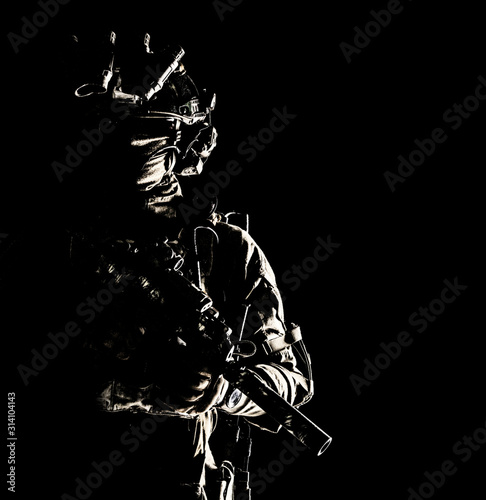 Army special operations forces soldier in mask and combat uniform, helmet equipped night-vision device, armed submachine gun with silencer, looking aside, low key studio portrait on black, copyspace photo