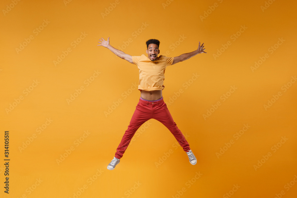 Funny young african american guy in bright casual clothes posing isolated on yellow orange background studio portrait. People lifestyle concept. Mock up copy space. Jumping spreading hands and legs.