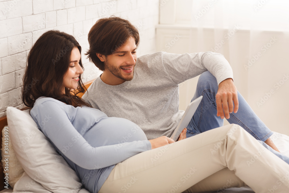 Pregnant woman and her husband using digital tablet together at home