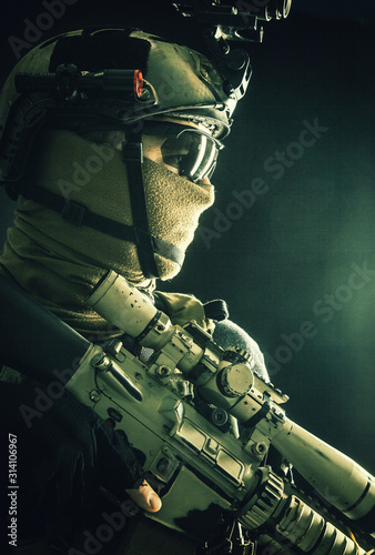 Shoulder portrait of army elite troops sniper, anti-terrorist tactical team marksman wearing helmet with thermal imager, hiding face behind mask, armed rifle with optical scope, studio shoot on black photo