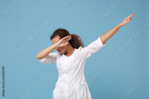 African american doctor woman isolated on blue background in studio. Female doctor in white medical gown showing DAB dance gesture. Healthcare personnel health medicine concept. Mock up copy space.
