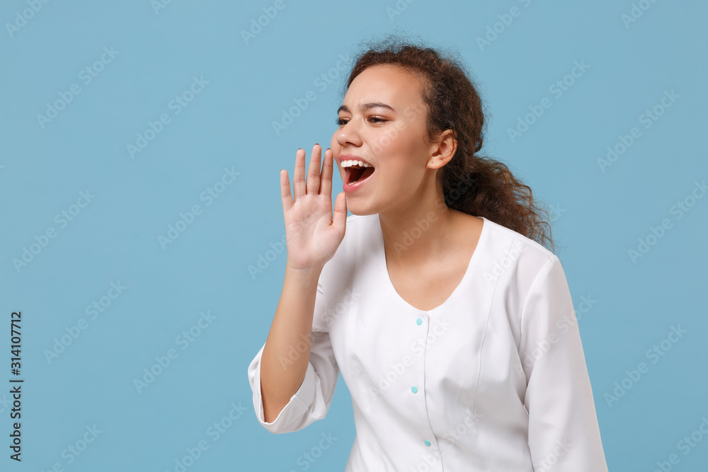 African american doctor woman isolated on blue background. Female doctor in white medical gown screaming with hand gesture near mouth. Healthcare personnel health medicine concept. Mock up copy space. African american doctor woman isolated on blue background. Female doctor in white medical gown screaming with hand gesture near mouth. Healthcare personnel health medicine concept. Mock up copy space.