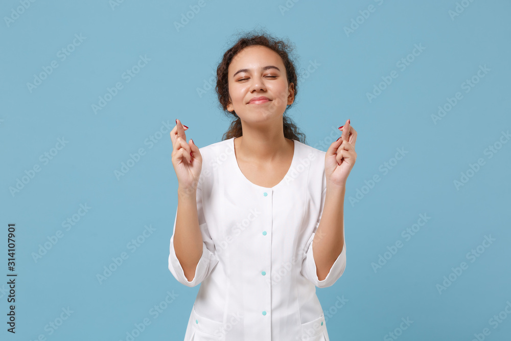 African american doctor woman isolated on blue background. Female doctor in medical gown keep fingers crossed eyes closed making wish. Healthcare personnel health medicine concept. Mock up copy space. African american doctor woman isolated on blue background. Female doctor in medical gown keep fingers crossed eyes closed making wish. Healthcare personnel health medicine concept. Mock up copy space.