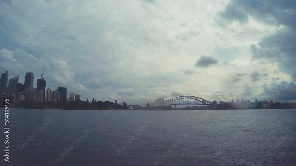 Sydney Harbour Bridge Time Lapse & Sydney Opera House Skyline. Cloudscape Shot In New South Wales Australia From Royal Botanical Gardens On Rainy Day Over Seawater With Cloudy Stormy Sky Sydney Harbour Bridge Time Lapse & Sydney Opera House Skyline. Cloudscape Shot In New South Wales Australia From Royal Botanical Gardens On Rainy Day Over Seawater With Cloudy Stormy Sky