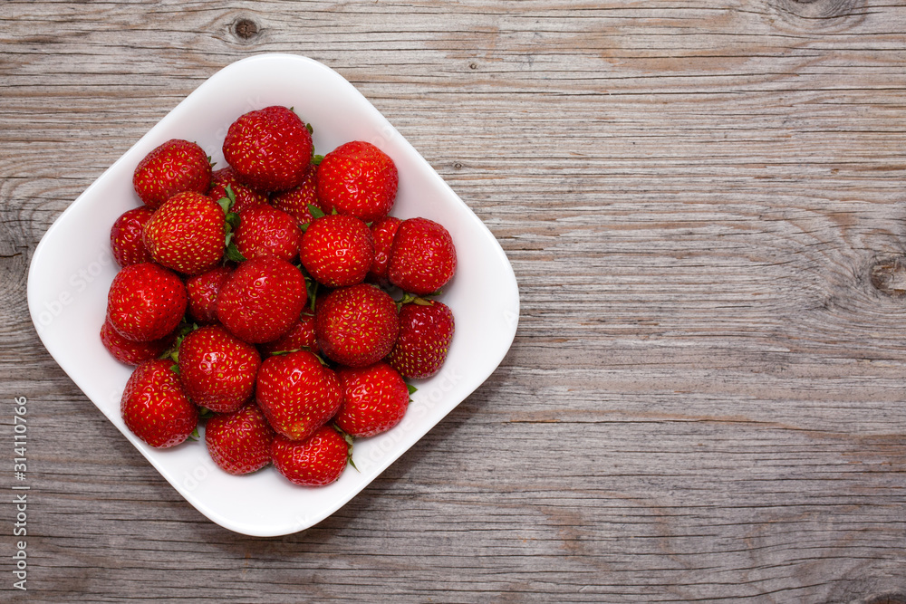 Strawberries berries in a white plate on a wooden background. Free copy space for text. Close up, top view Strawberries berries in a white plate on a wooden background. Free copy space for text. Close up, top view