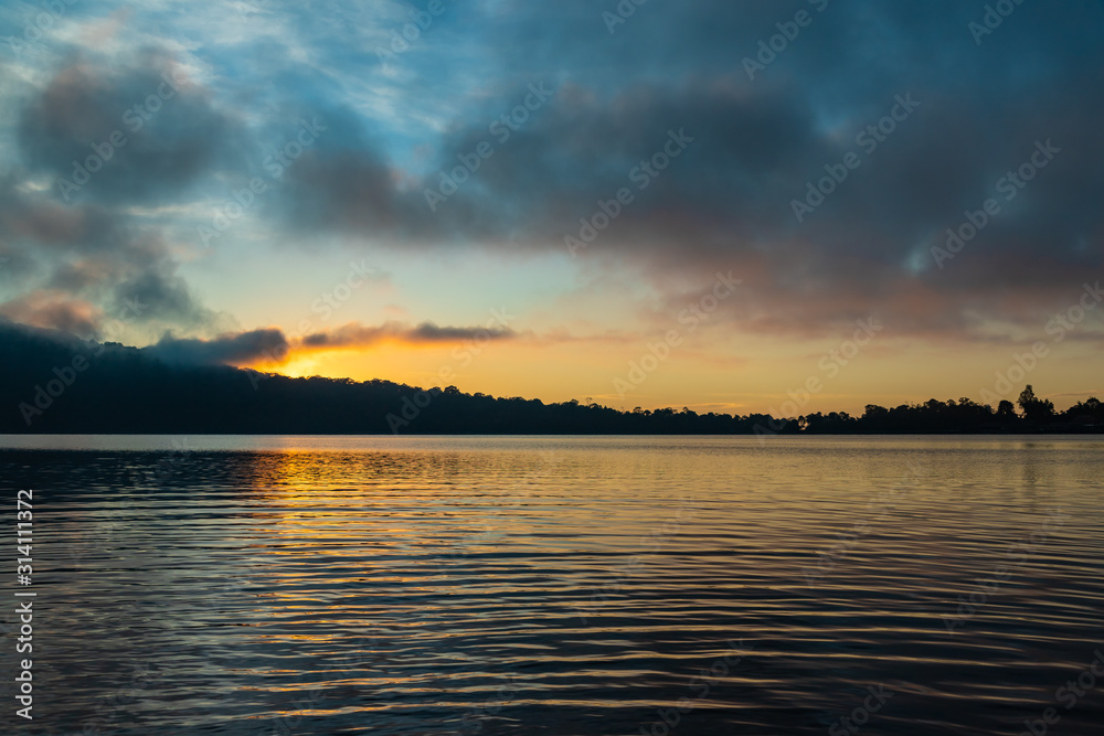 A beautiful sunrise at a Lake Bratan. Bali island, Indonesia. Yellow sky with clouds.