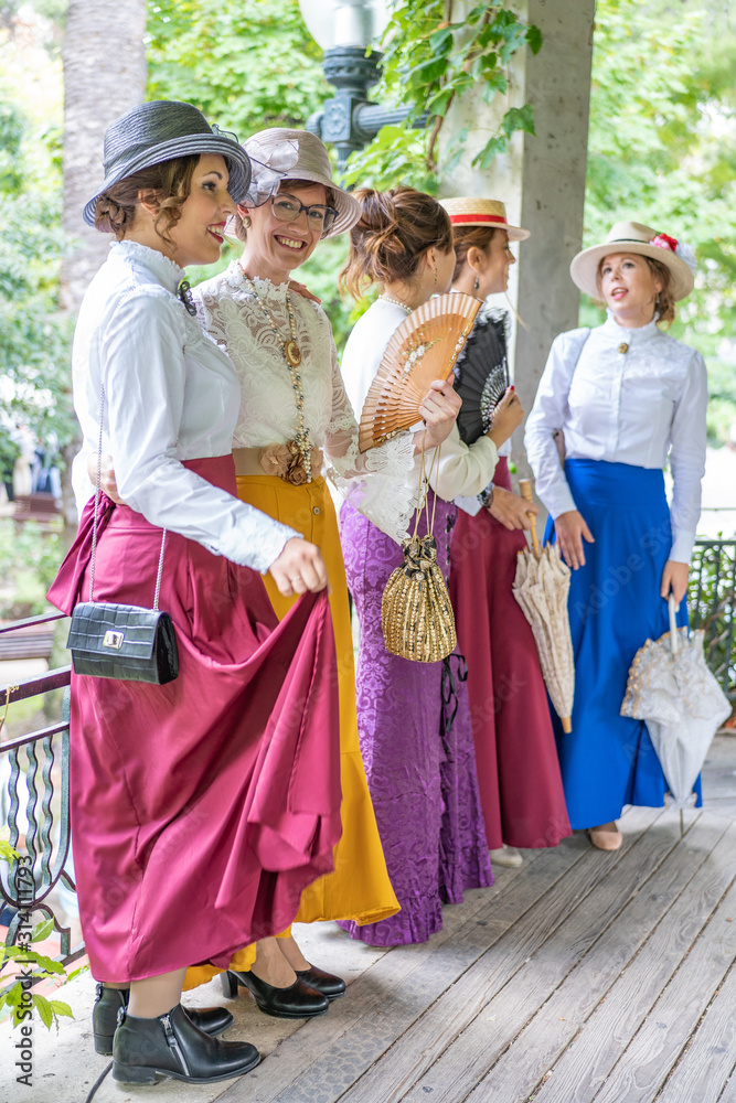 group of five friends dressed in vintage clothes and umbrellas and fans laughing and having fun together