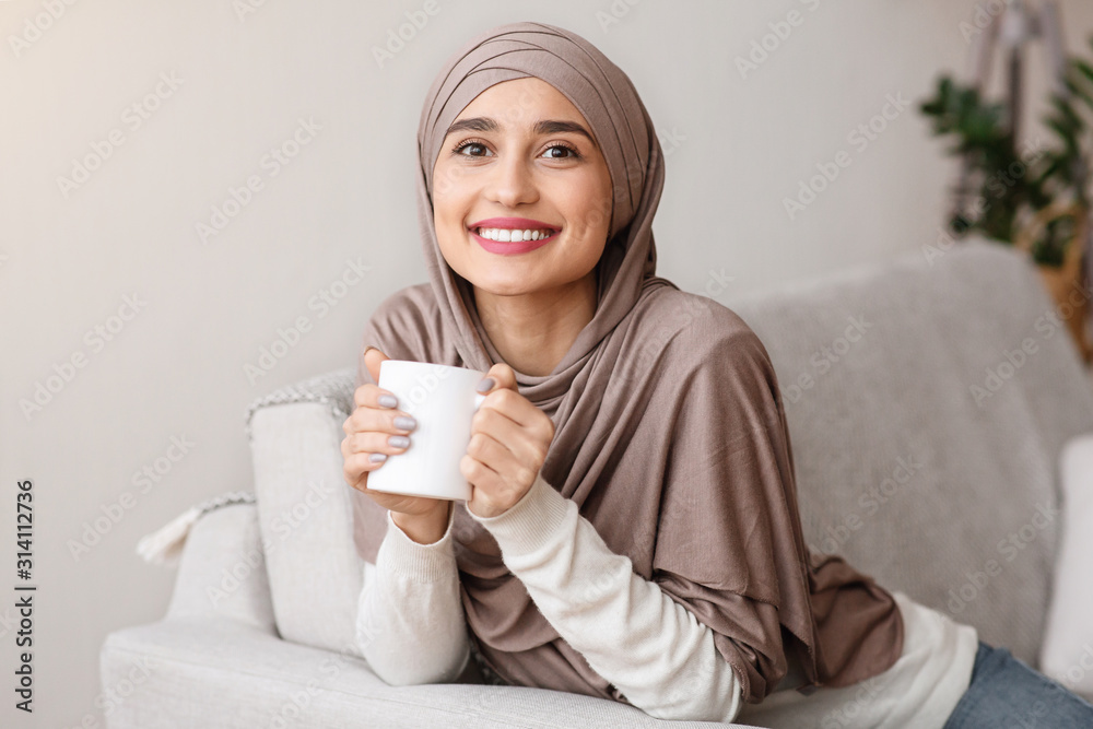 Happy muslim girl in hijab relaxing with tea at home Happy muslim girl in hijab relaxing with tea at home
