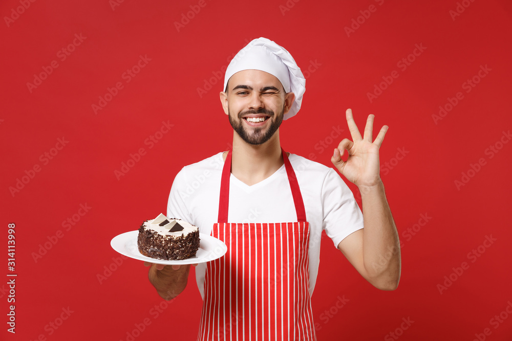 Bearded male chef cook or baker man in striped apron white t-shirt toque chefs hat posing isolated on red background. Cooking food concept. Mock up copy space. Hold plate with cake showing OK gesture. - obrazy, fototapety, plakaty 