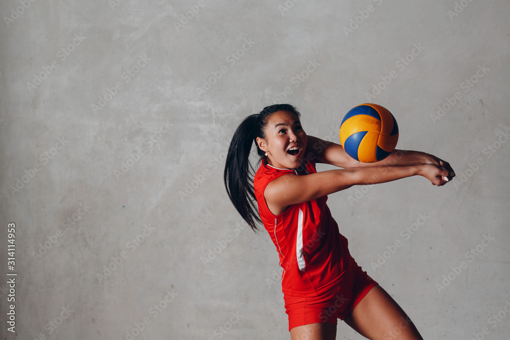 © primipil - Young smiling Asian woman volleyball player in red uniform with ball