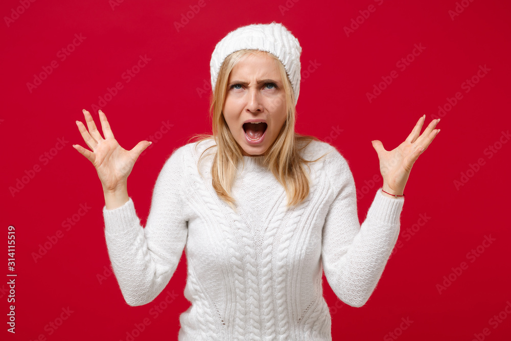 Crazy young woman in white sweater hat isolated on red wall background studio portrait. Healthy fashion lifestyle people emotions, cold season concept. Mock up copy space. Spreading hands, screaming. Crazy young woman in white sweater hat isolated on red wall background studio portrait. Healthy fashion lifestyle people emotions, cold season concept. Mock up copy space. Spreading hands, screaming.