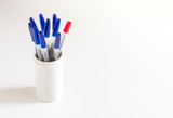 one red ballpoint pen among many blue ballpoint pens on a white background in a white glass