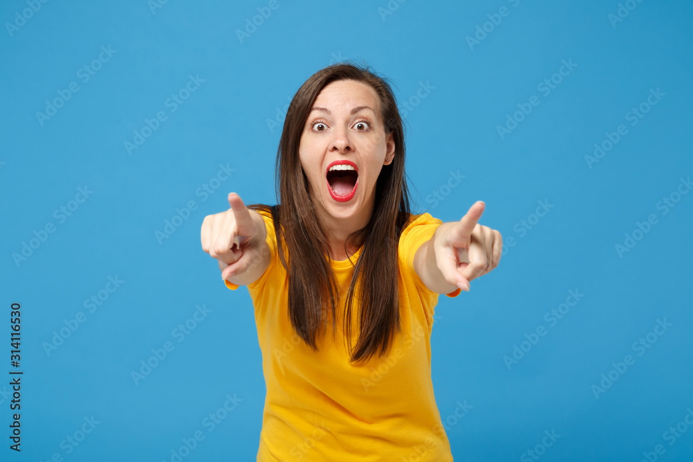 Excited young brunette woman girl in yellow t-shirt posing isolated on bright blue wall background, studio portrait. People lifestyle concept. Mock up copy space. Pointing index fingers on camera. Excited young brunette woman girl in yellow t-shirt posing isolated on bright blue wall background, studio portrait. People lifestyle concept. Mock up copy space. Pointing index fingers on camera.