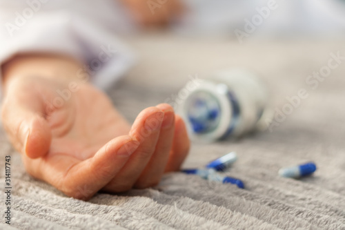 Woman’s hand close up committing suicide by overdosing on medication, pills and bottle beside. Overdose pills and addict concept background.