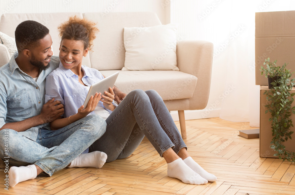 Afro Spouses Using Tablet Sitting On Floor In New Flat Afro Spouses Using Tablet Sitting On Floor In New Flat