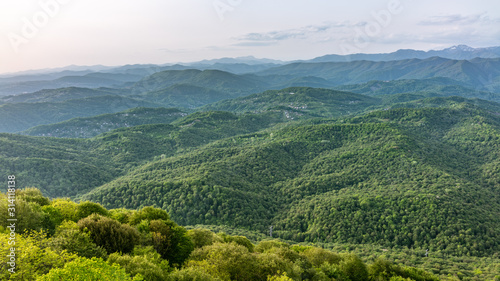 Layers of mountains in the haze during sunset. Beautiful sunset in the mountains. Beautiful sunset in a green hilly valley with villages and fog in the lowlands.