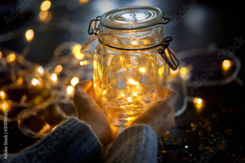 Transparent glass jar with Christmas lights in someone's hands