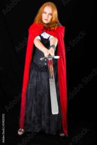 halloween girl wearing in black long gown and red robe brandishing twohanded sword (focus on sword) photo