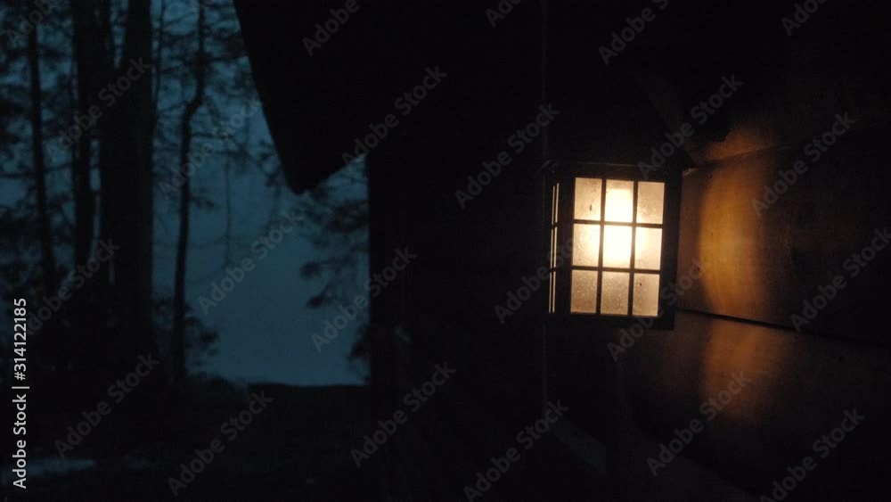 Lantern Glowing at Cabin by Lake at Night