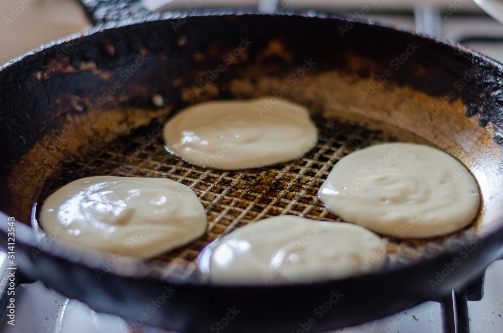 Frying fritters in a pan. Four raw pancakes in a hot pan. Raw yeast dough. Traditional cuisine. Selective focus. - obrazy, fototapety, plakaty 