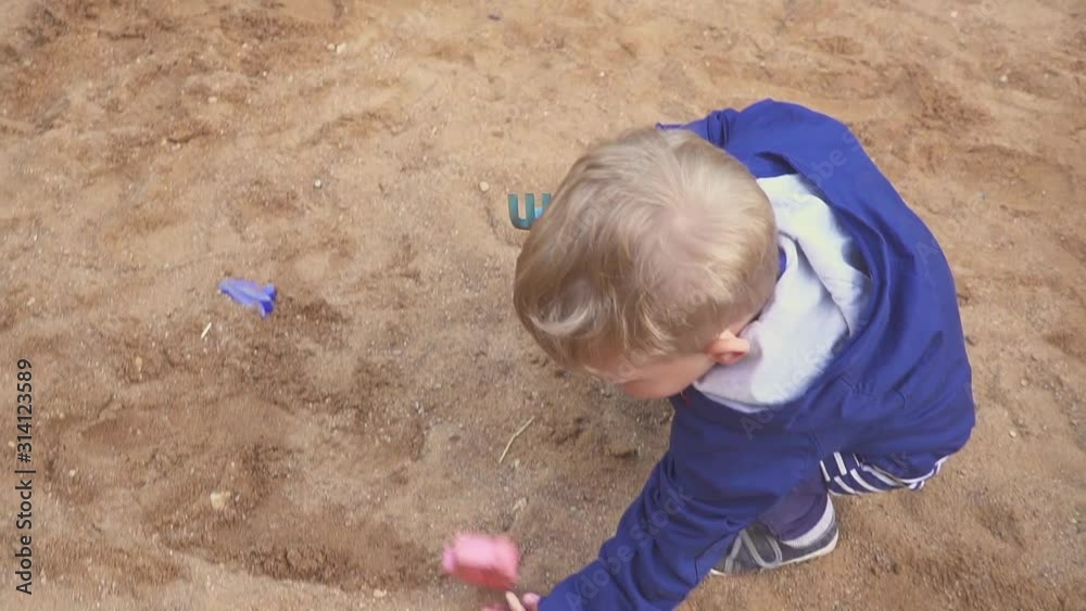 Kids Games. Baby boy digging in the sandbox. Smiles and touches the sand. Kids Games. Baby boy digging in the sandbox. Smiles and touches the sand.