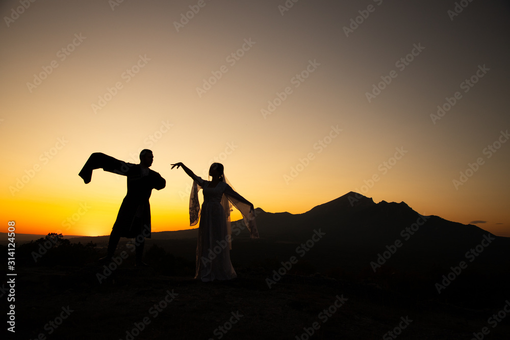 Couple dancing a national dance on a background of mountains at sunset