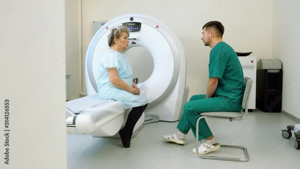 Doctor talking to elderly female patient. Aged woman is undergoing MRI or CT scan in modern hospital. 4K Doctor talking to elderly female patient. Aged woman is undergoing MRI or CT scan in modern hospital. 4K