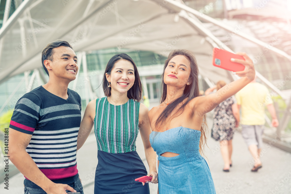Obraz premium Three asian friends walking along the city taking selfies. Tourism and holiday concept