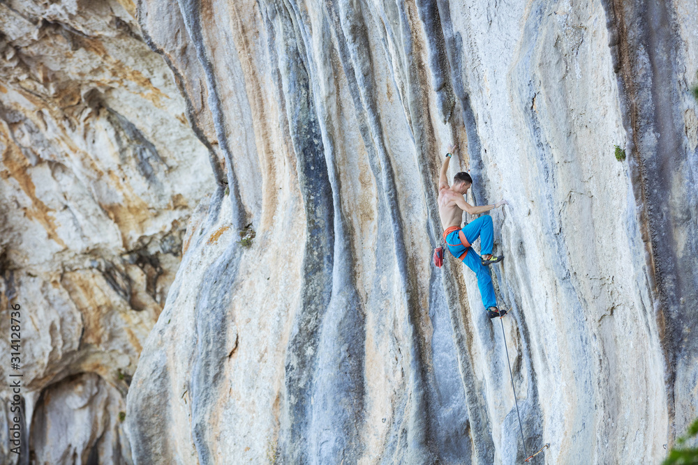 Fototapeta premium Caucasian young man climbing challenging route on cliff