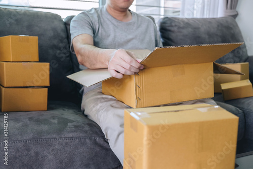 Small business parcel for shipping, Happy man opening online shopping package box with parcel while sitting on sofa at home