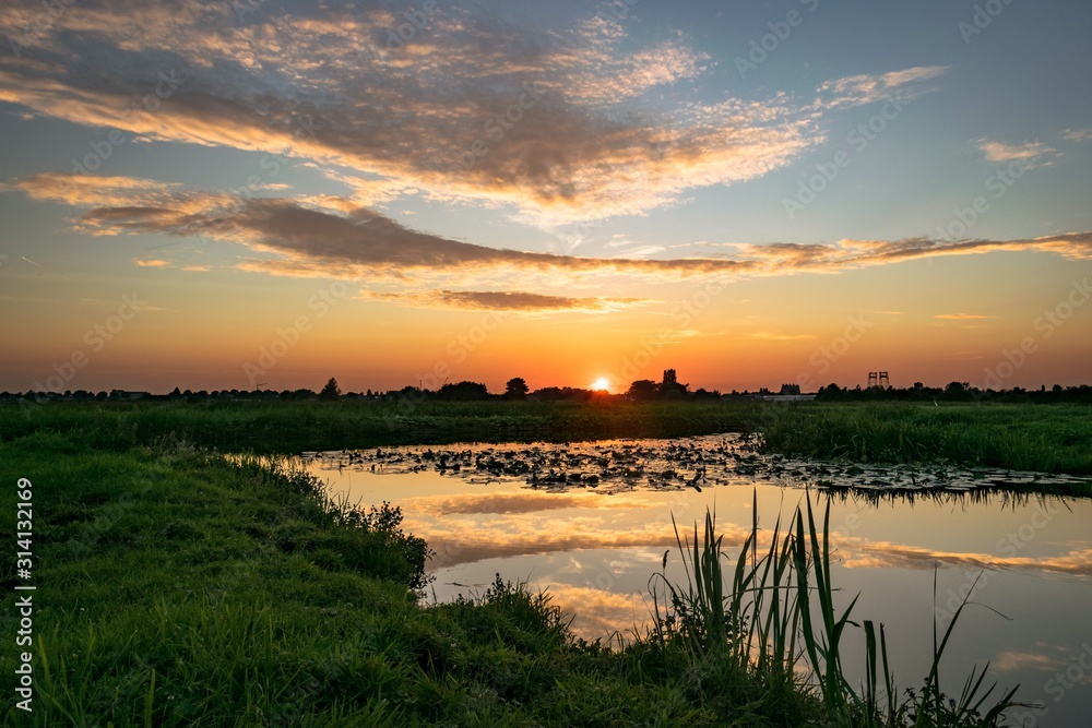 Sun goes down over the polder landscape in Holland. Beautiful colors and reflections in the water.