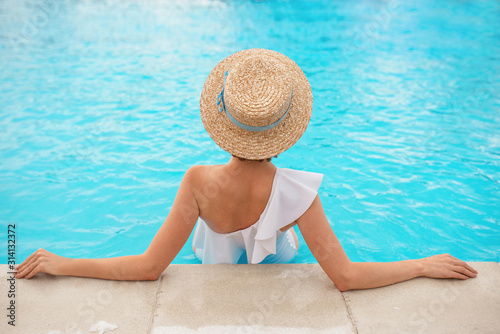 beautiful redhead (ginger) woman's back in the white swimminig suit sitting by the swimming pool (or sea or ocean) in the straw hat in summer day. Summer, relax, wellness, recreation concept photo