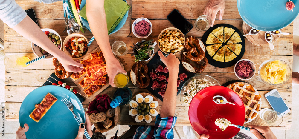 Above view of wooden trendy table full of friends people and home made food to celebrate and stay together having fun in friendship - concept of caucasian men and women mixed ages - obrazy, fototapety, plakaty 
