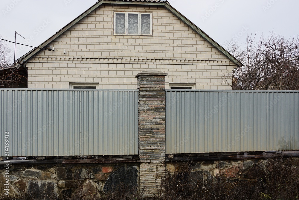 part of a long gray fence of metal and stones on the street in front of a rural brick house part of a long gray fence of metal and stones on the street in front of a rural brick house