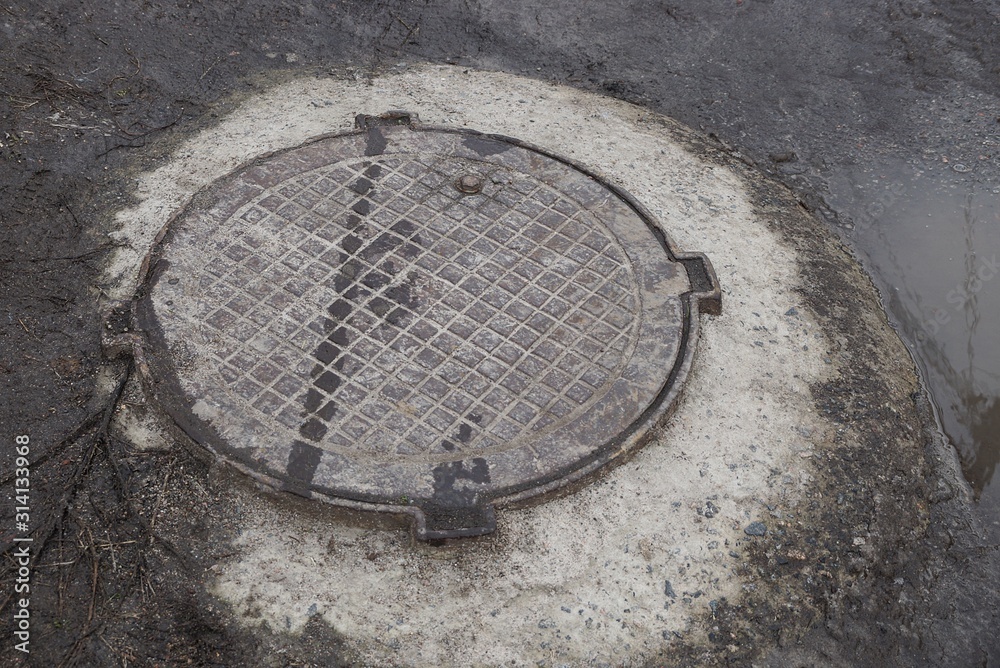 one iron brown sewer manhole on gray concrete on wet ground and water outside