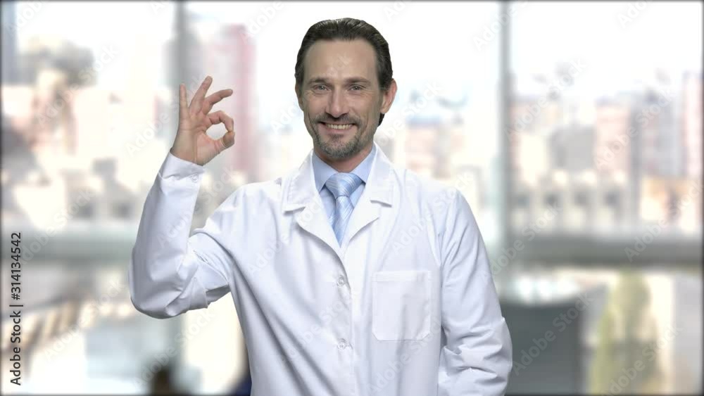 Lab technician showing ok sign. Smiling middle-aged man in white robe looking at camera on blurred background. Lab technician showing ok sign. Smiling middle-aged man in white robe looking at camera on blurred background.