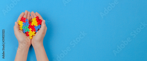 Kid hand holding colorful heart on light blue background. World autism awareness day concept photo