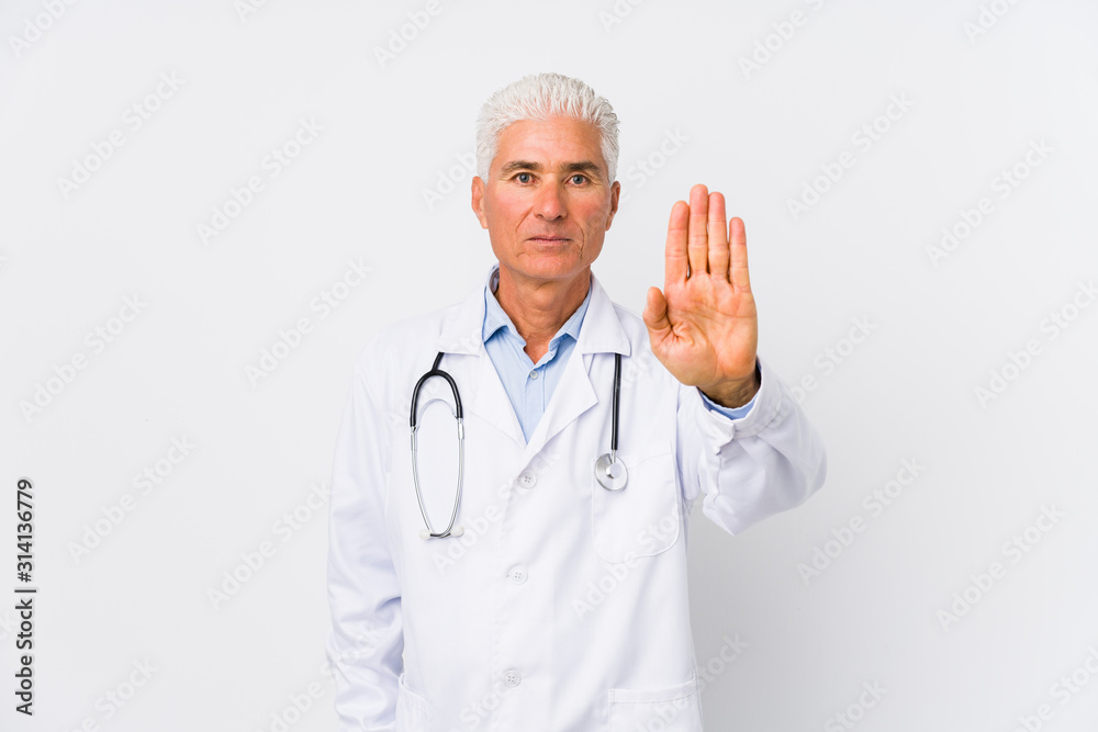Mature caucasian doctor man standing with outstretched hand showing stop sign, preventing you.