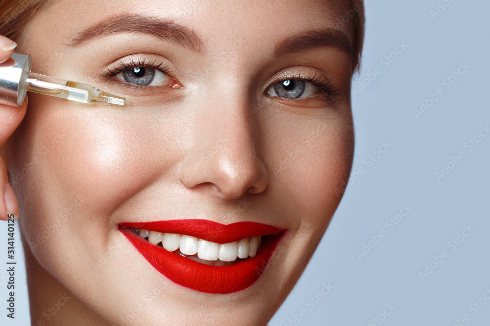 Beautiful girl with red lips and classic makeup with oil for skin in hand. Beauty face.