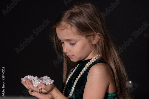 Fotografie Portrait of a beautiful little girl with a beads on a dark background