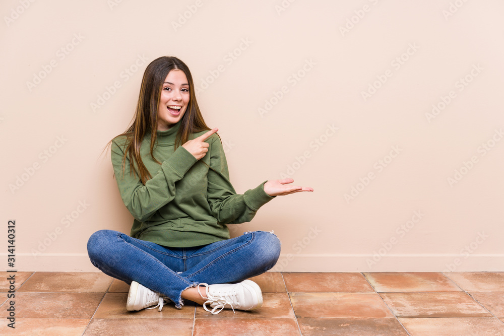 Young caucasian woman sitting on the floor isolated excited holding a copy space on palm. Young caucasian woman sitting on the floor isolated excited holding a copy space on palm.