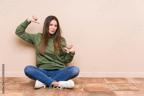 Young caucasian woman sitting on the floor isolated feels proud and self confident, example to follow.