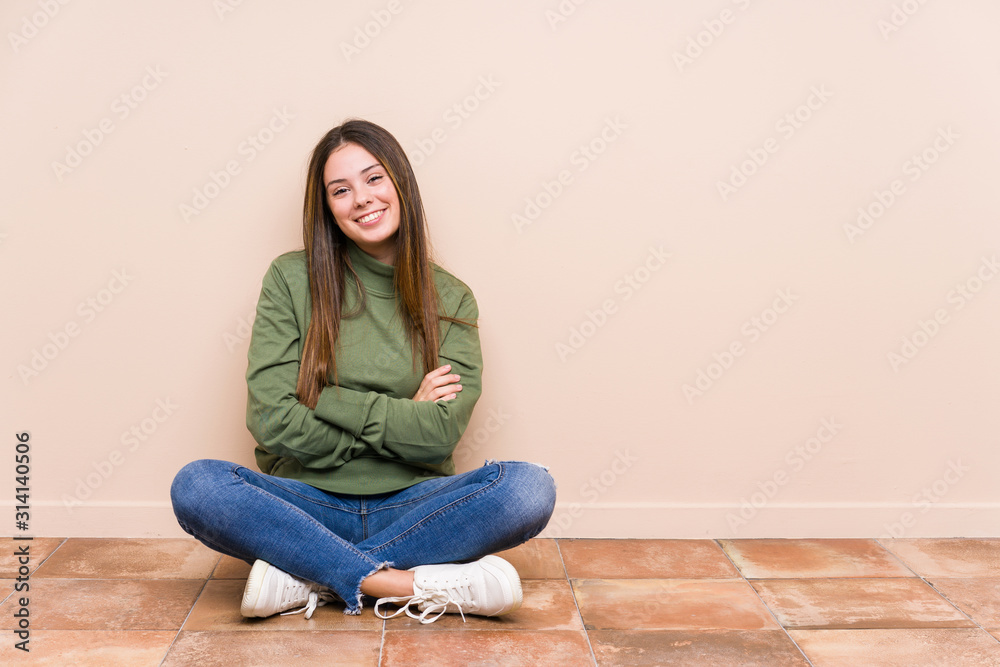 Young caucasian woman sitting on the floor isolated who feels confident, crossing arms with determination. Young caucasian woman sitting on the floor isolated who feels confident, crossing arms with determination.