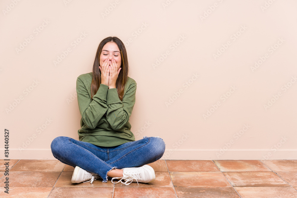 Young caucasian woman sitting on the floor isolated laughing about something, covering mouth with hands. Young caucasian woman sitting on the floor isolated laughing about something, covering mouth with hands.