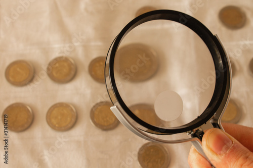 Man hand holding magnifying glass and looking at two euro coins located on a table. Copy space.