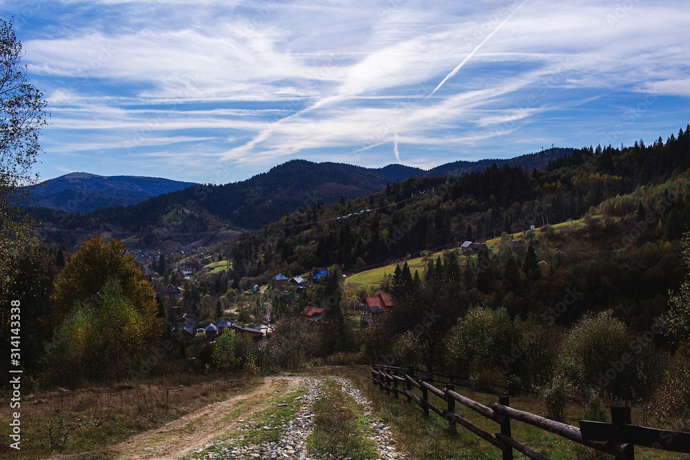 Autumn landscape: Carpathian mountains and village below, beautiful sky with cirrus clouds.
