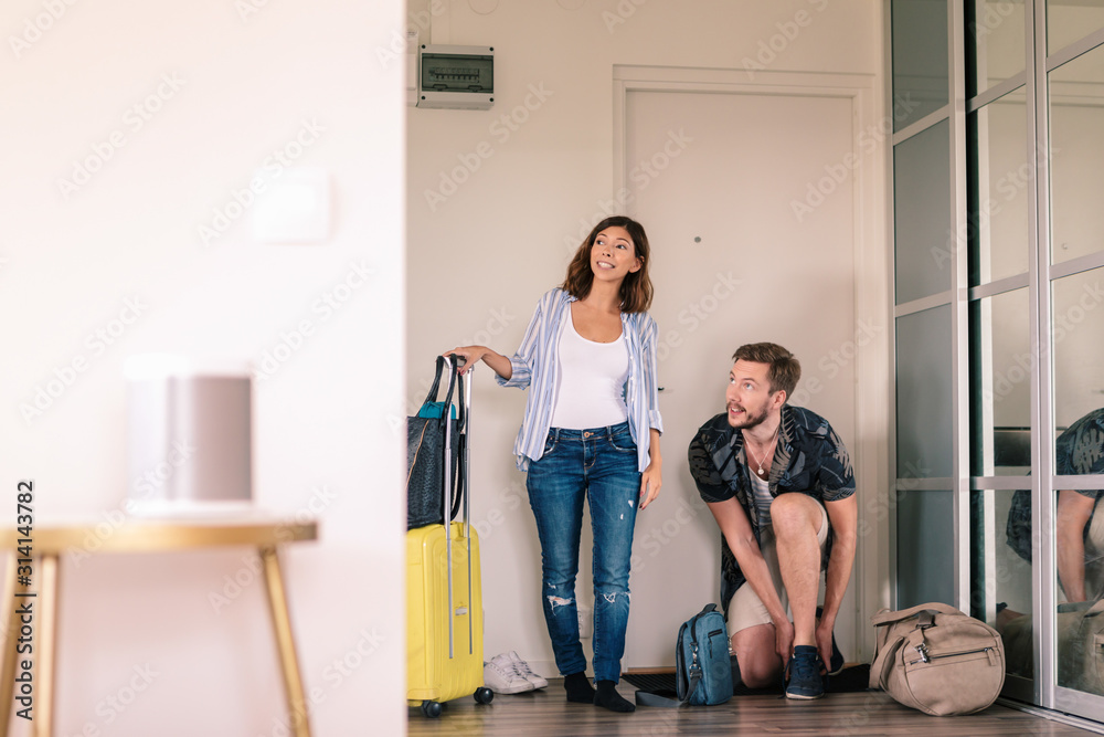 Excited couple with luggage removing shoes while looking around in apartment against doorway Excited couple with luggage removing shoes while looking around in apartment against doorway