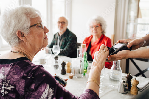 Cropped hand of owner holding credit card reader while senior woman paying in restaurant photo